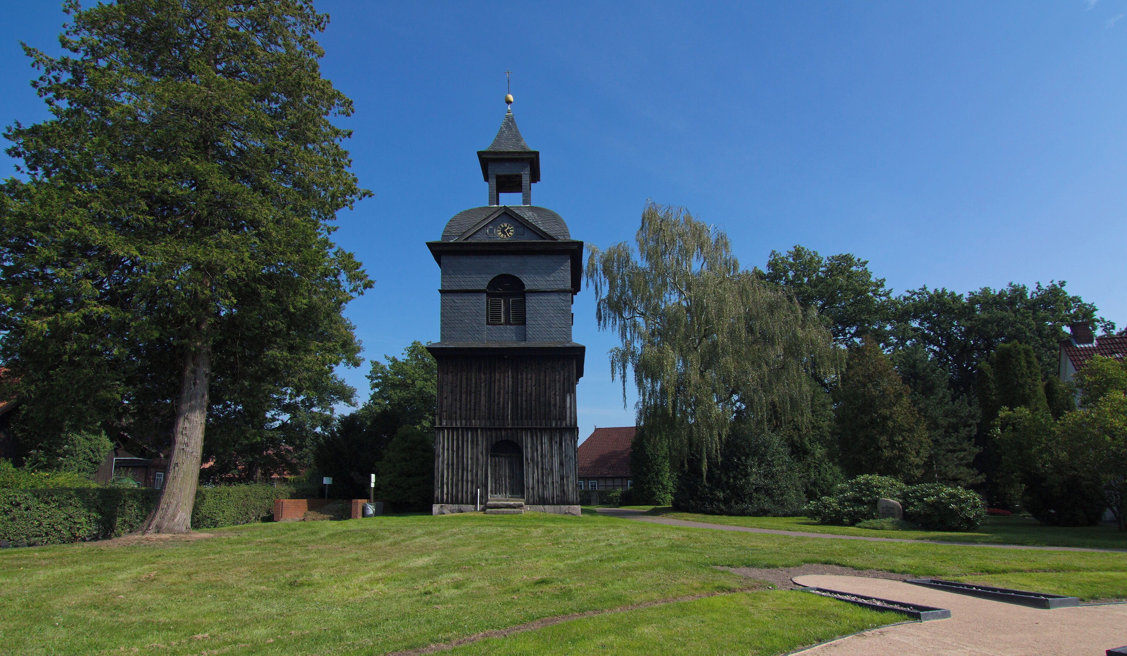 A historic church with a clock tower, surrounded by lush greenery and trees.