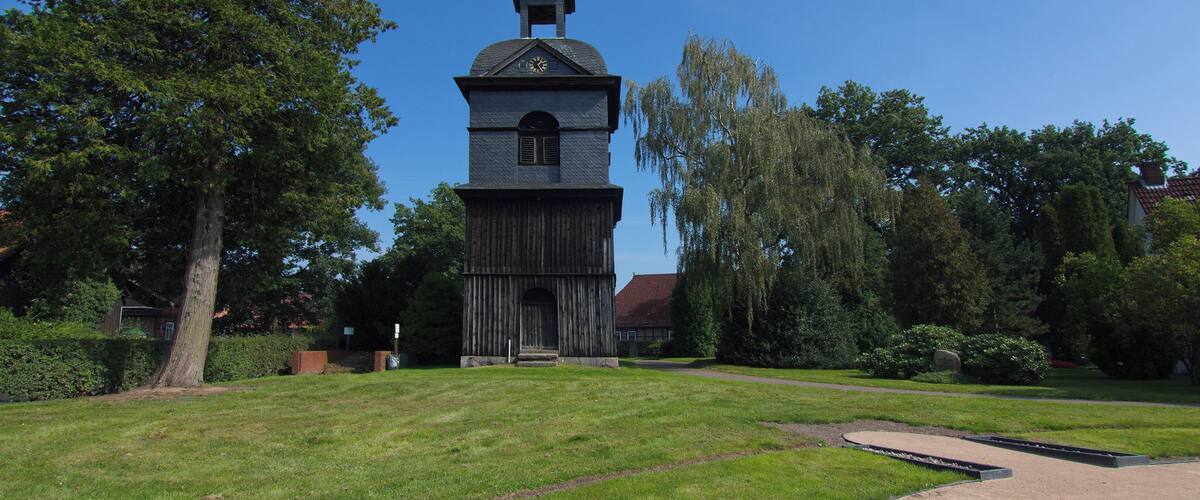 A historic church with a clock tower, surrounded by lush greenery and trees.