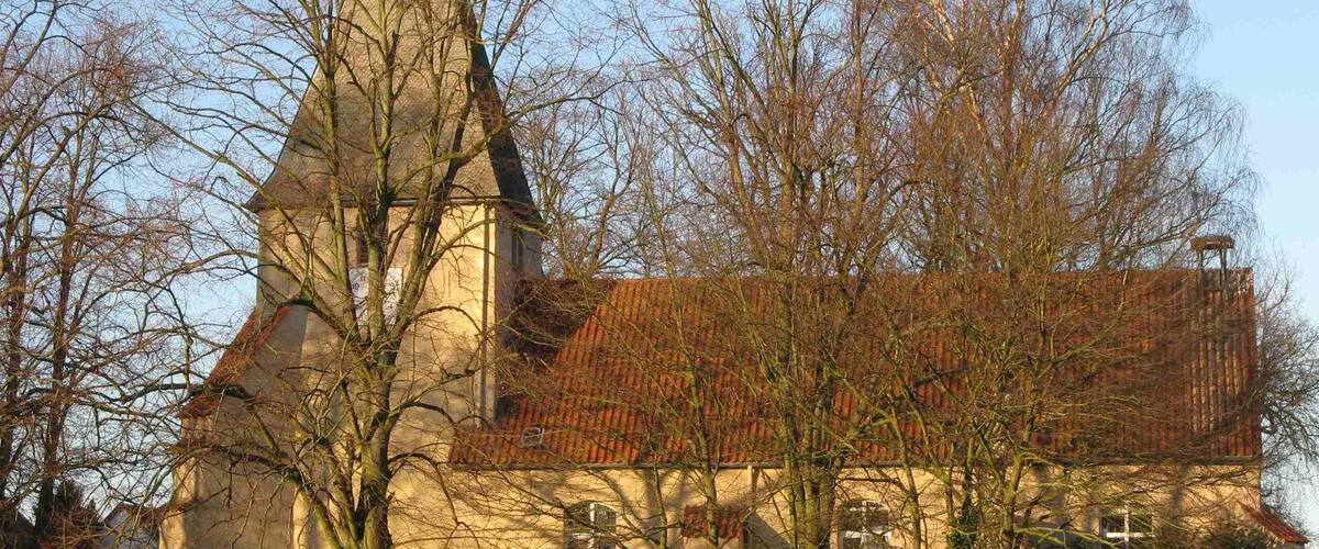 A church with a tall steeple and a red-tiled roof, surrounded by trees and a well-maintained lawn.