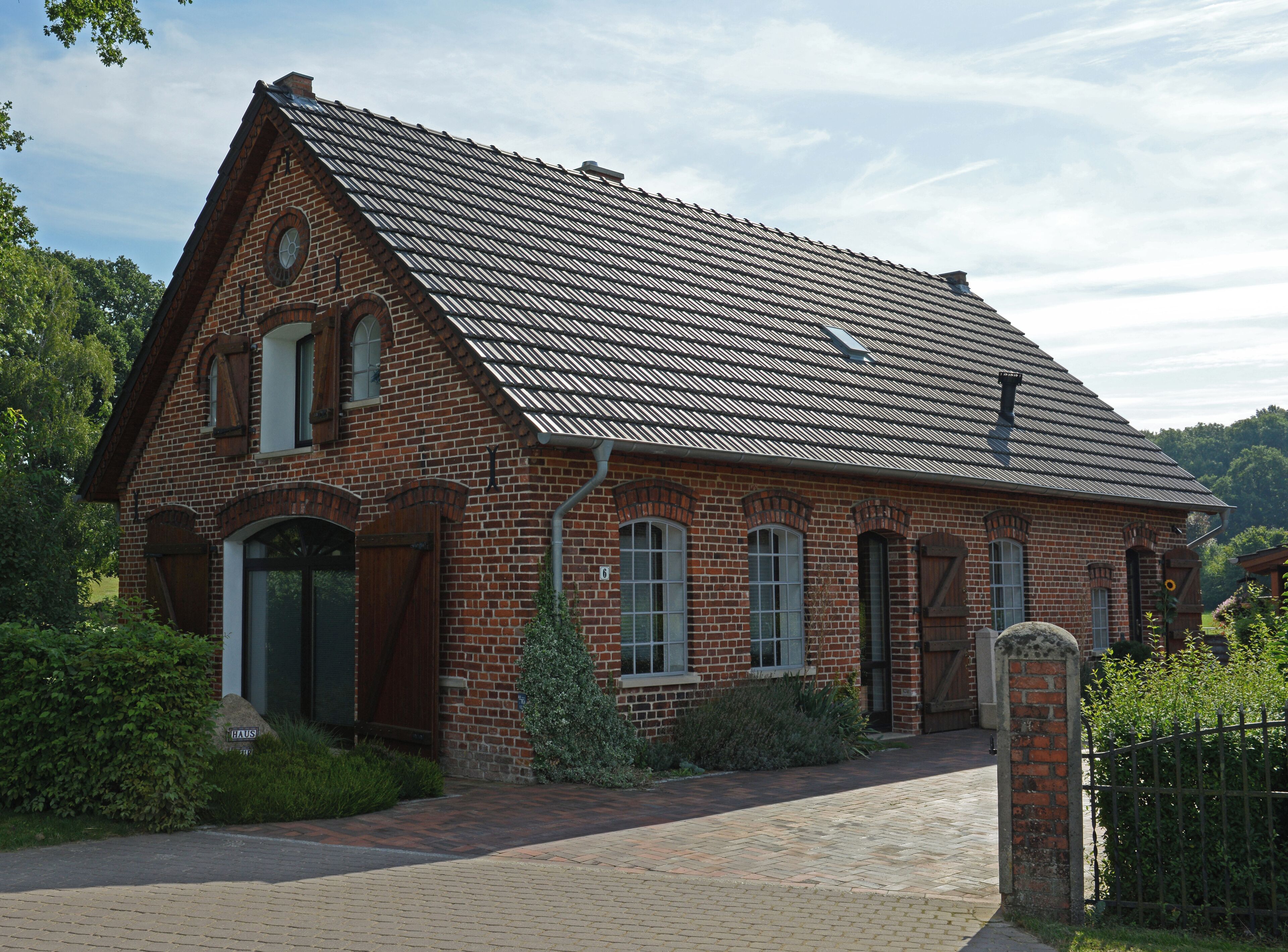 A brick house with a steeply pitched roof, a wooden gate, and a brick pathway leading to the entrance.