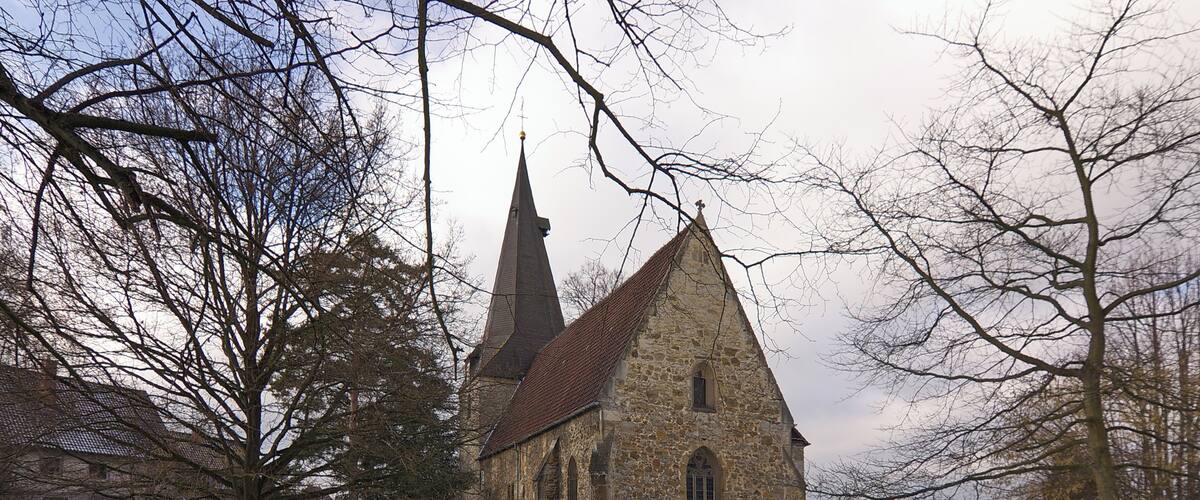 A stone church with two spires, surrounded by bare trees and a snow-covered ground.