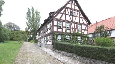 A traditional half-timbered house with a cobblestone pathway and a hedge.