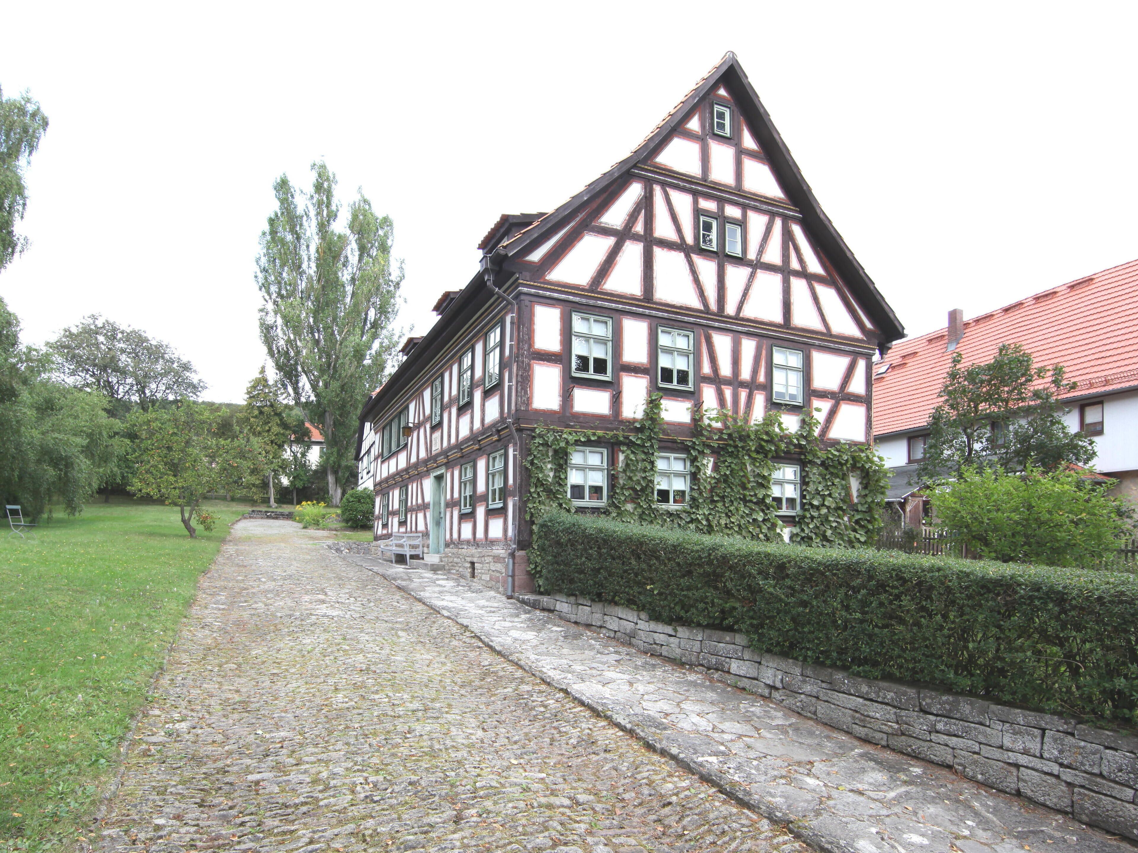 A traditional half-timbered house with a cobblestone pathway and a hedge.