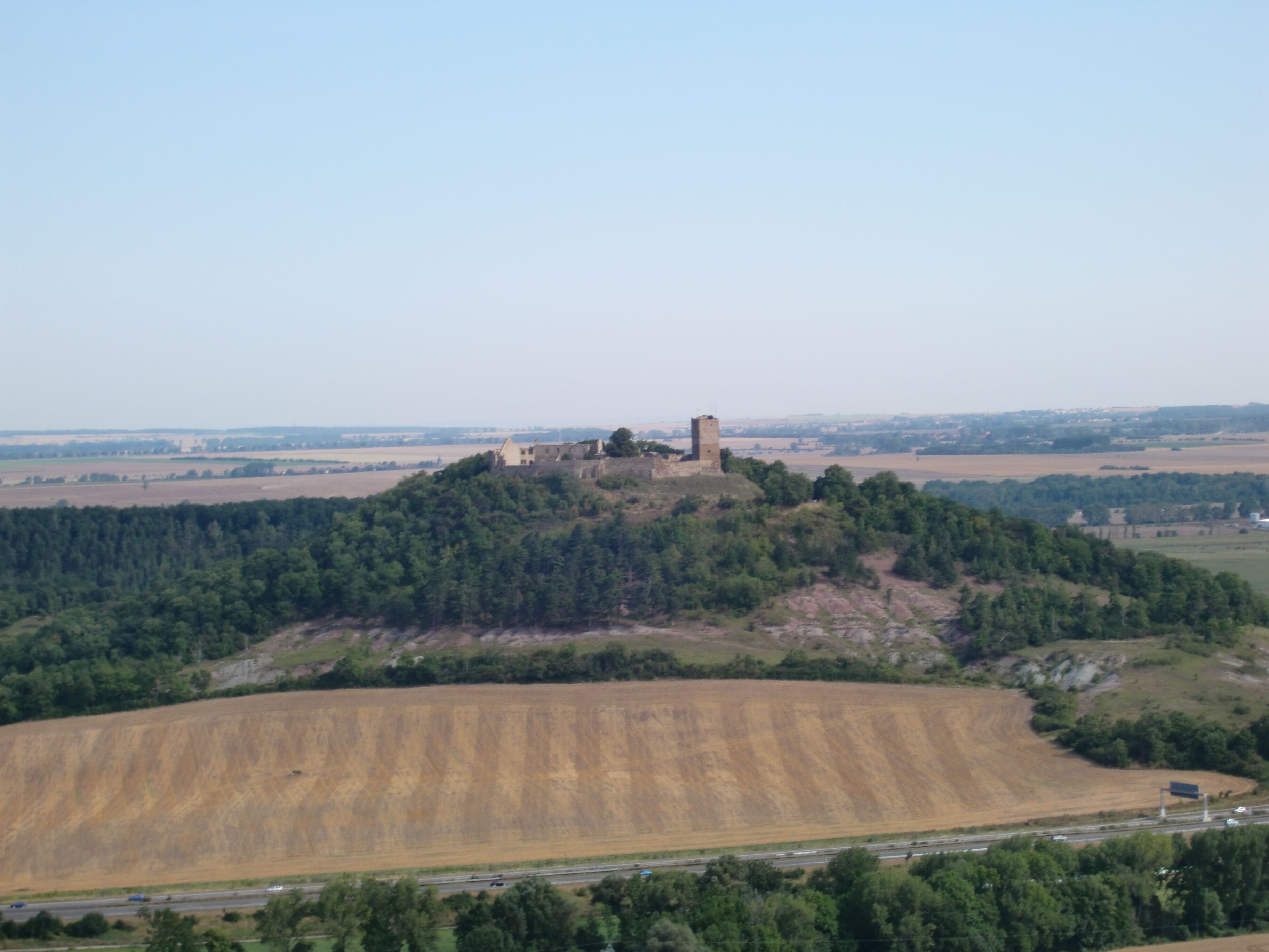 A hilltop castle surrounded by forest and fields.