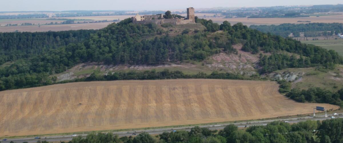 A hilltop castle surrounded by forest and fields.