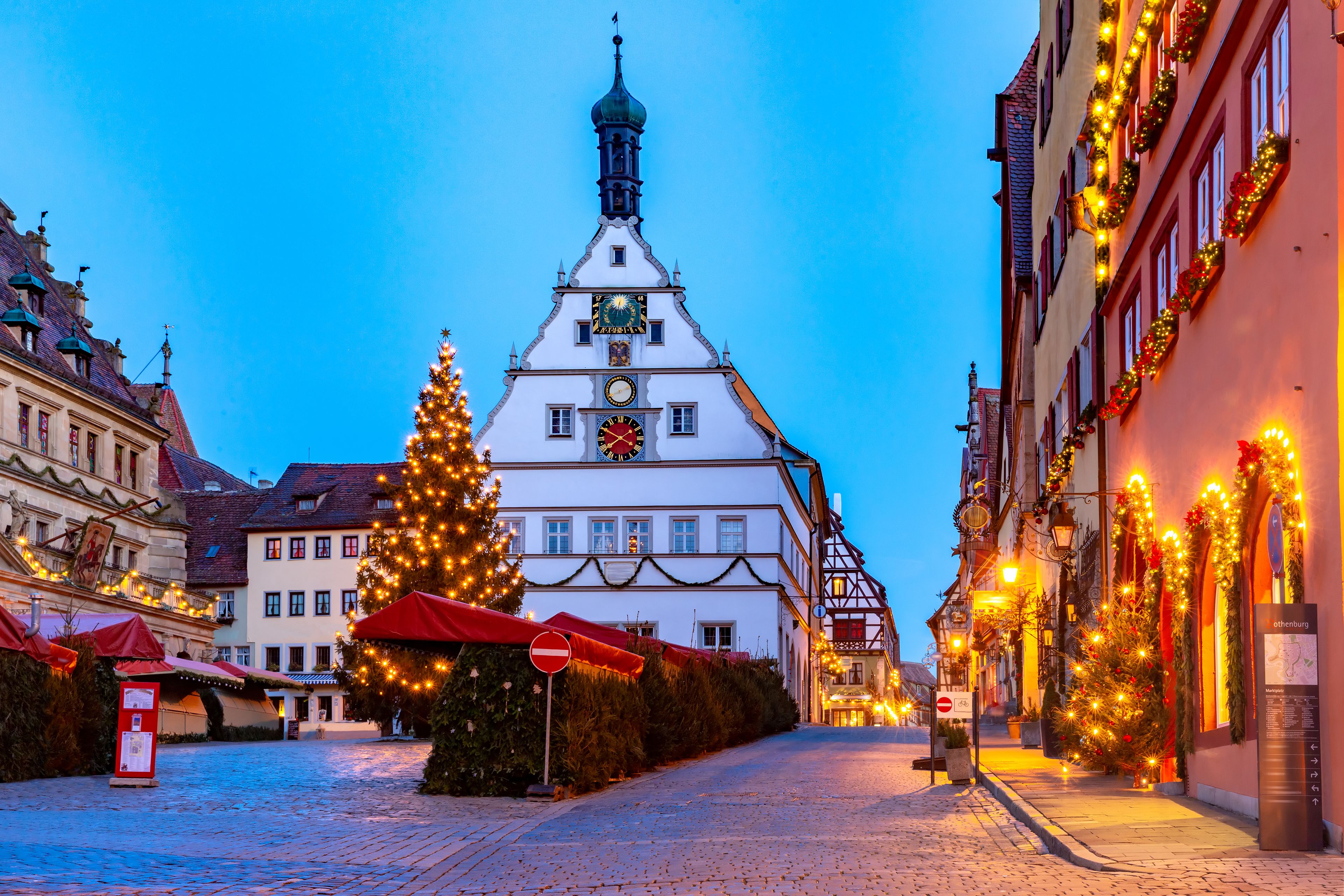 Una calle adoquinada flanqueada por edificios decorados con luces navideñas y un gran árbol de Navidad adornado.