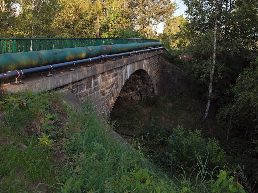 Uma ponte de pedra com canos de metal e guarda-corpo verde.