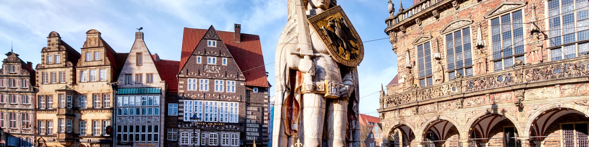 Ein historischer Platz mit einer markanten Statue, traditioneller europäischer Architektur und Kopfsteinpflaster.