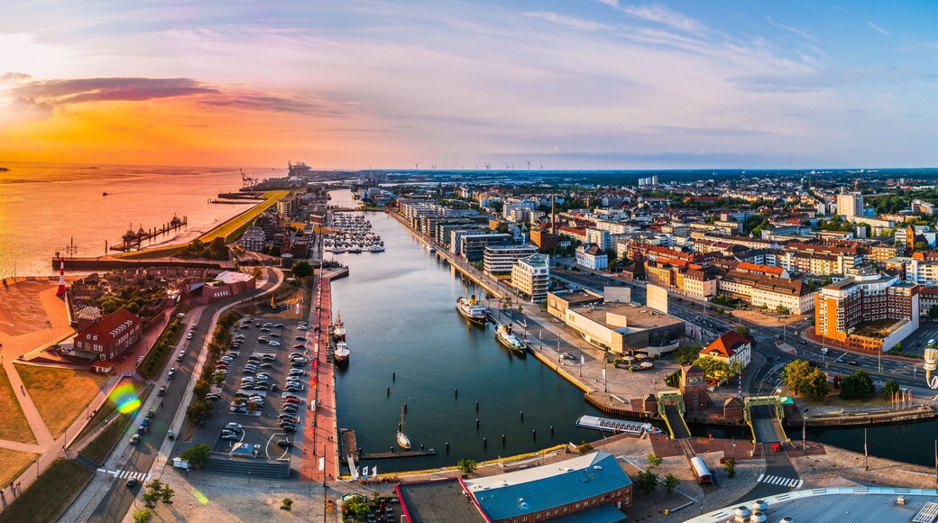A coastal cityscape with a marina, a lighthouse, and a sunset over the water.