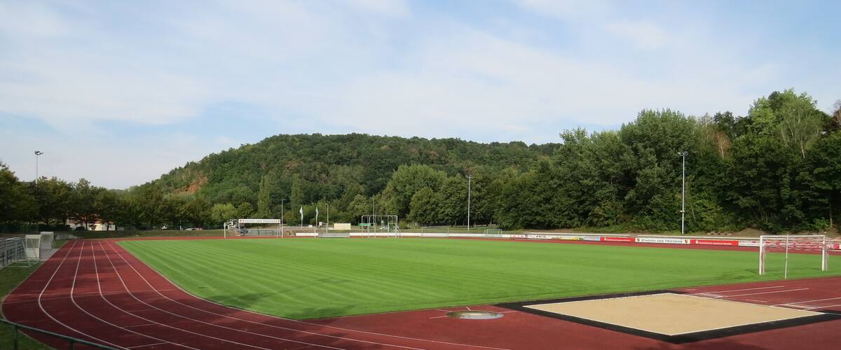 A running track with a red surface, a green field, and a hill in the background.
