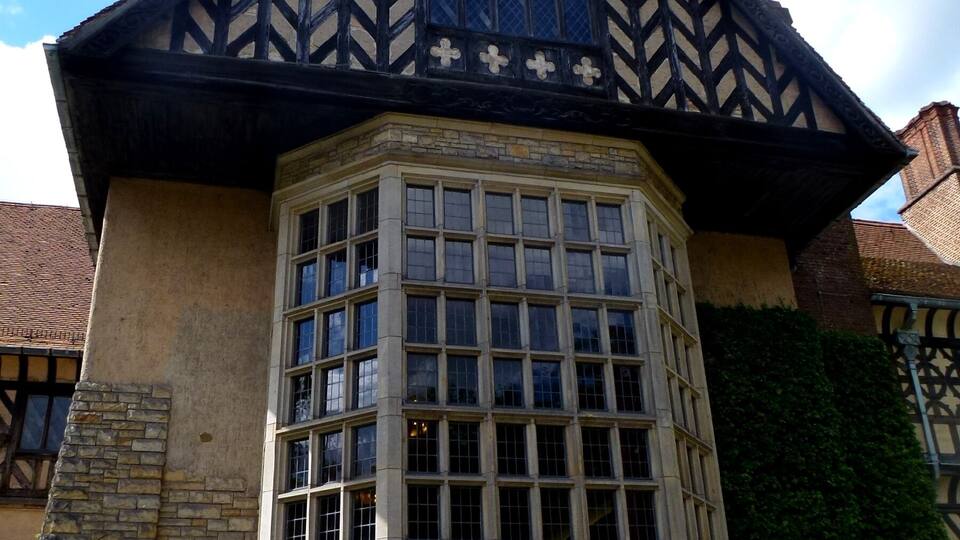 Um edifício histórico com telhado em estilo Tudor, grandes janelas e paredes de pedra.