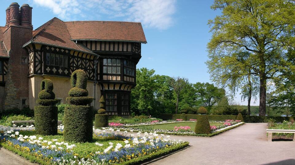 Um edifício em estilo Tudor com um jardim, apresentando sebes bem aparadas e uma variedade de flores.