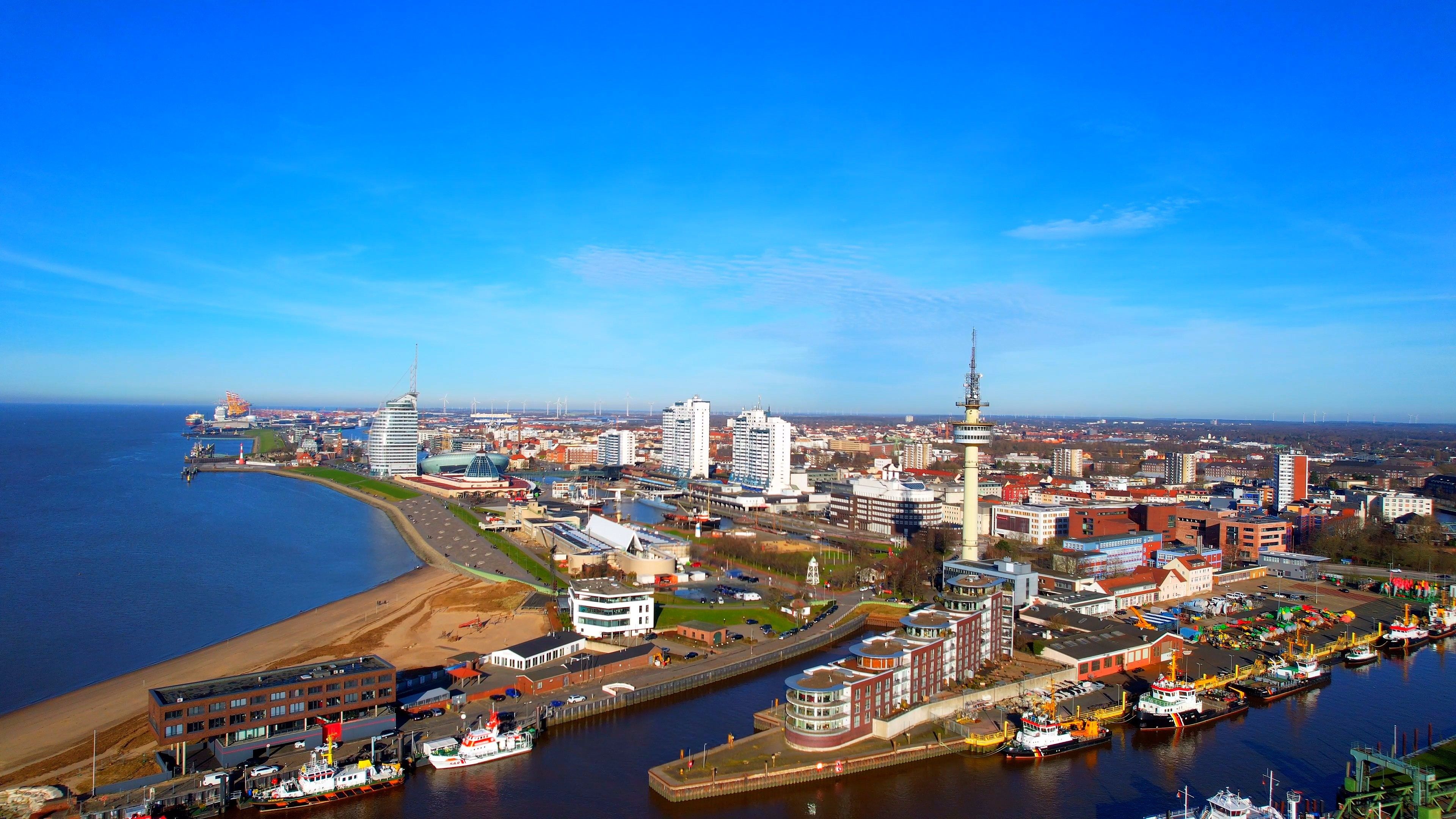 A coastal cityscape with a prominent tower, a marina with boats, and a mix of modern and traditional architecture.