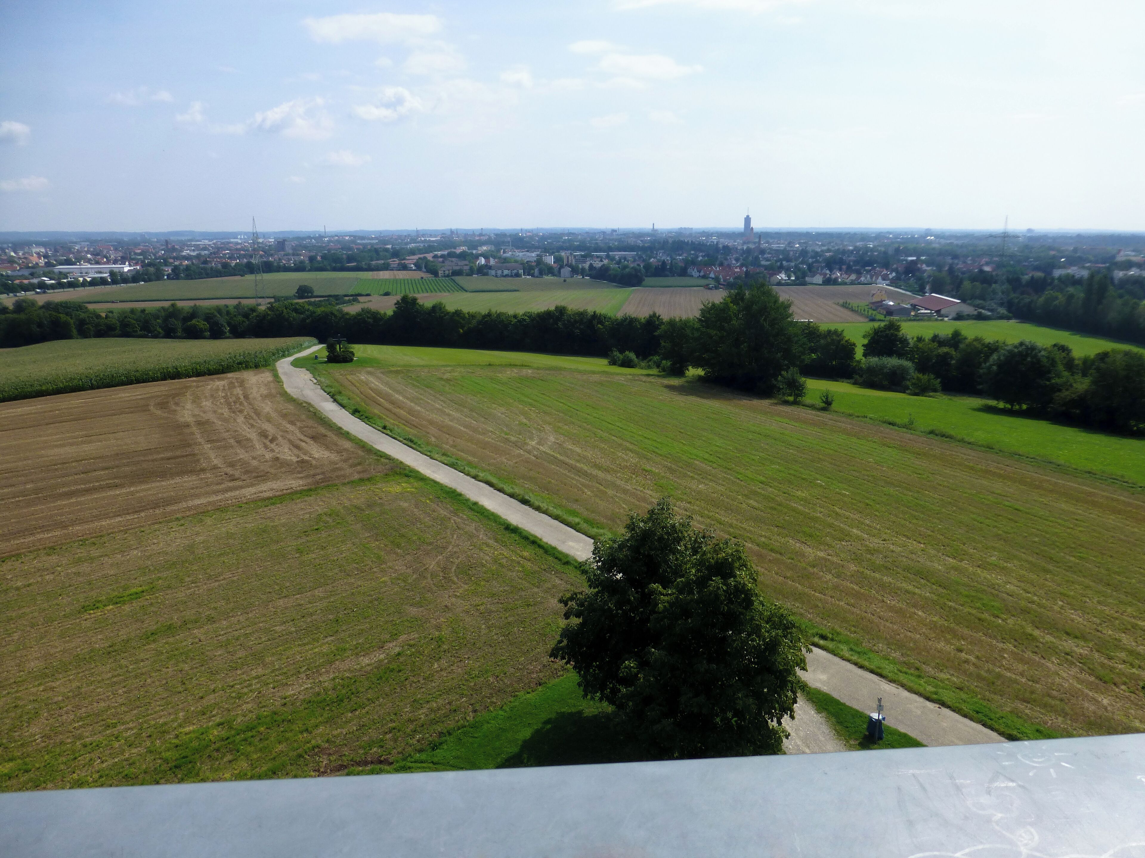 A rural landscape with fields, a winding road, and a distant city skyline.