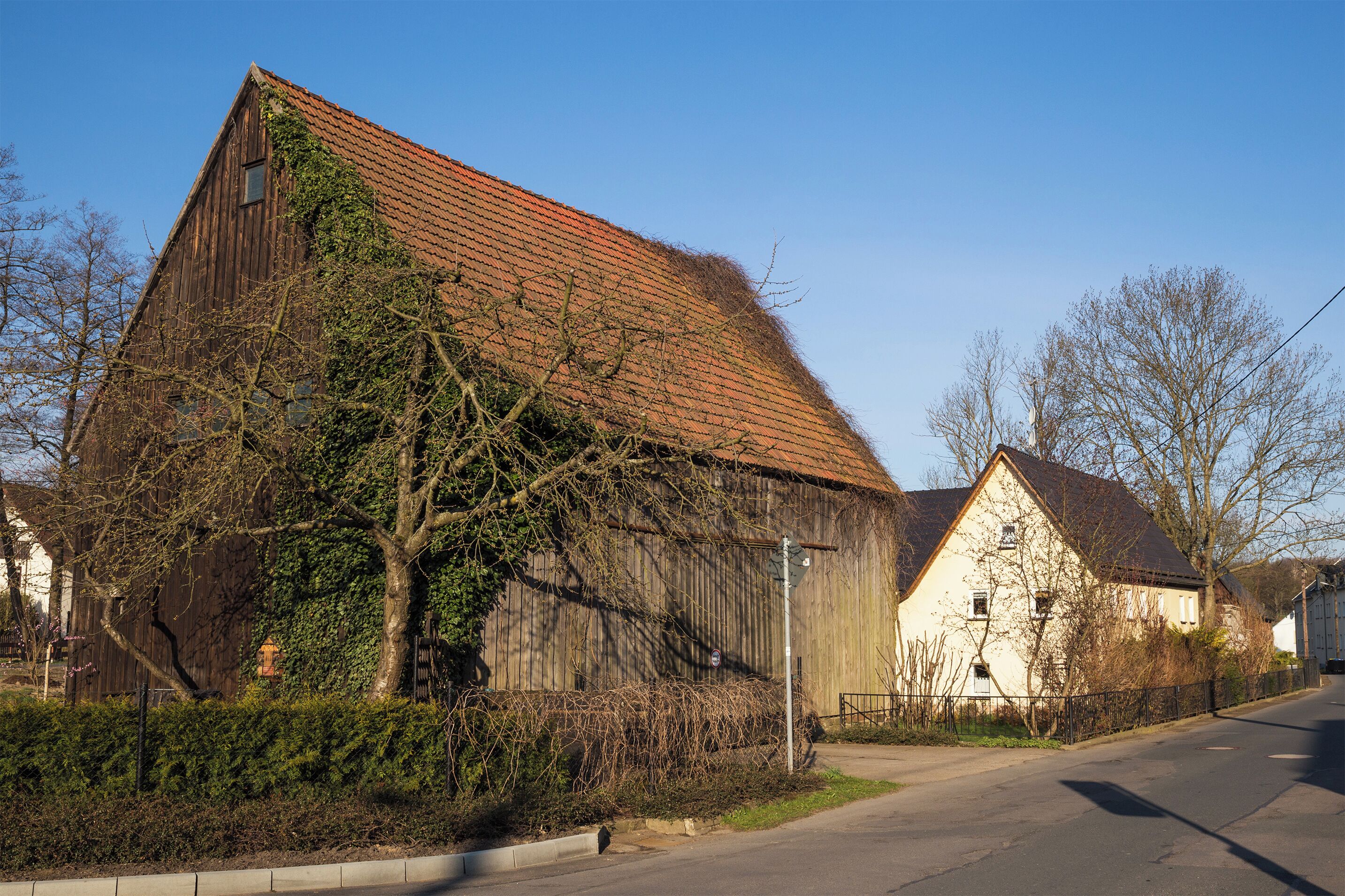 A rustic barn with a red roof, surrounded by trees and a clear blue sky.