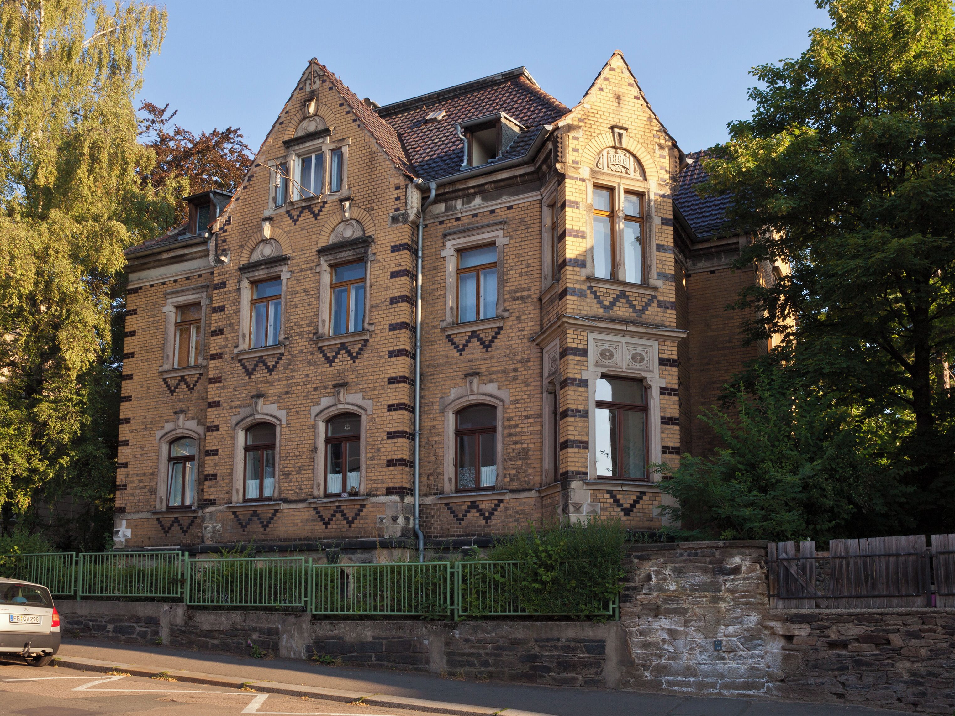 A historic brick building with ornate windows and a green metal fence.