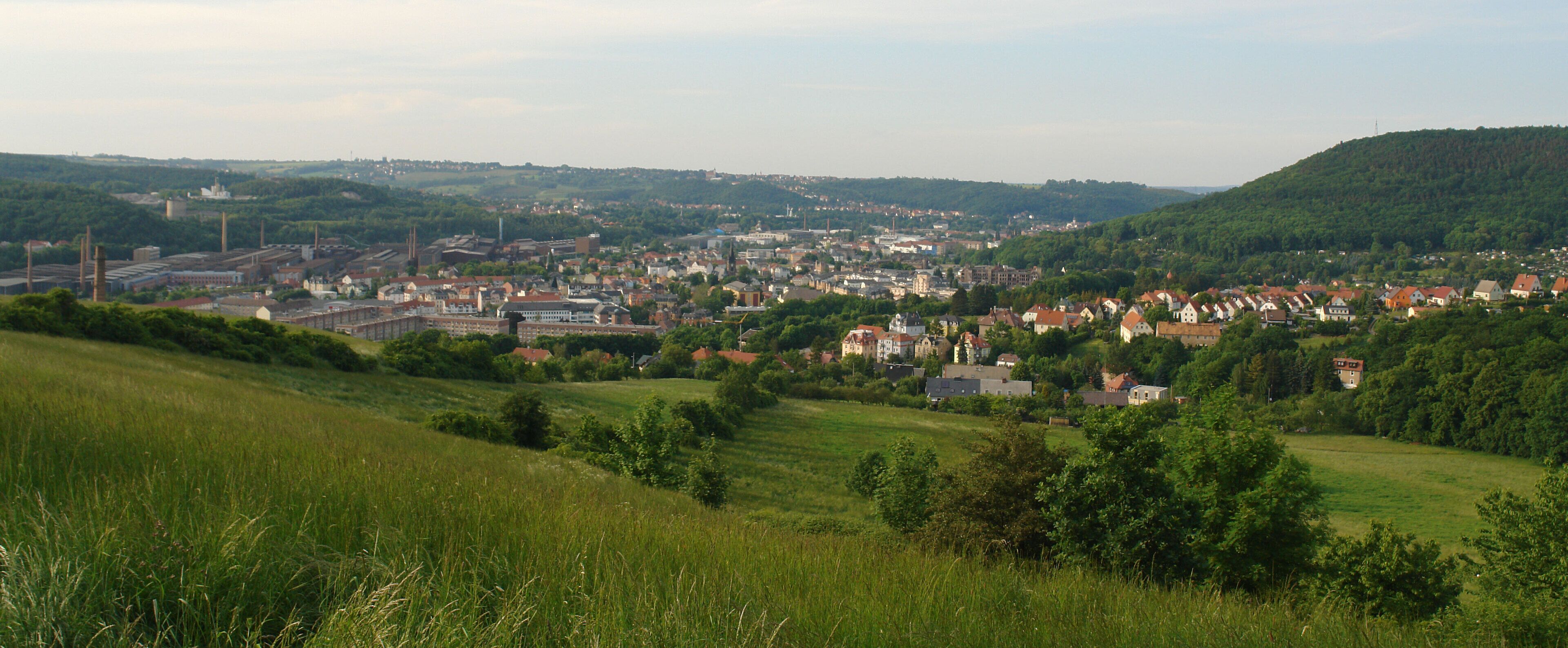 A town nestled in a valley with rolling hills, surrounded by greenery and featuring a mix of residential and industrial buildings.