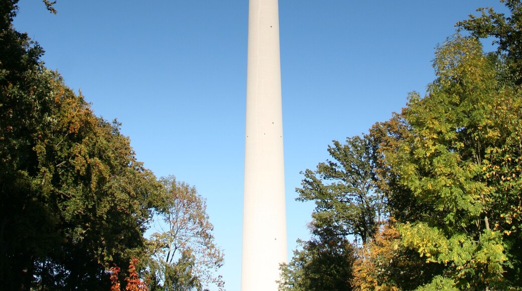 Una alta torre blanca con una antena roja y blanca en la parte superior, rodeada de árboles.