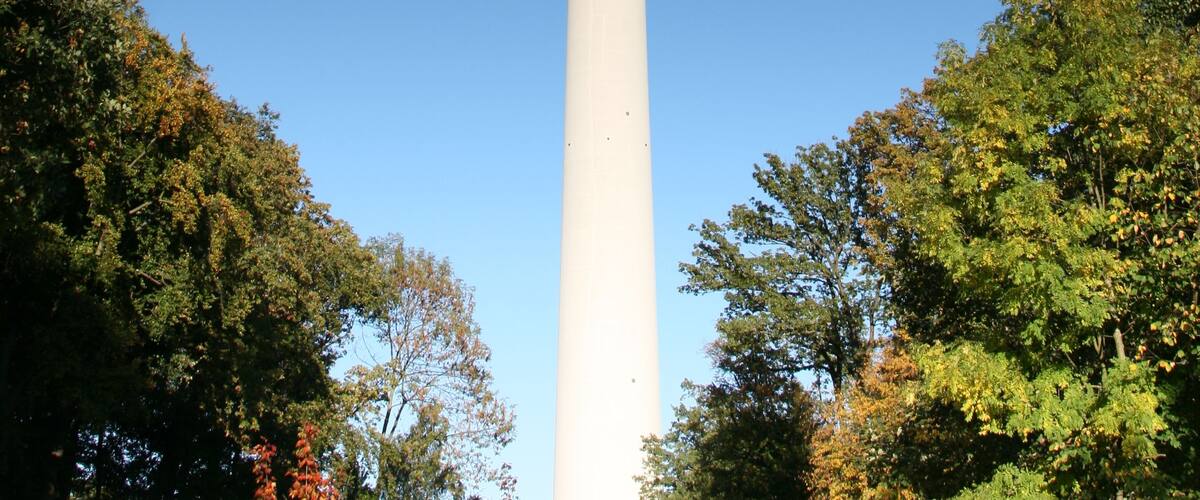 Ein hoher, weißer Turm mit einer rot-weißen Antenne, umgeben von Bäumen.