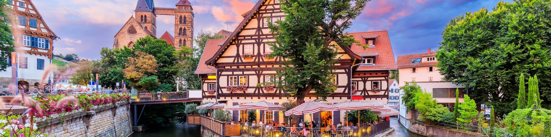 Eine Stadt am Flussufer mit traditionellen Fachwerkhäusern, einem Kirchturm und einer Brücke.