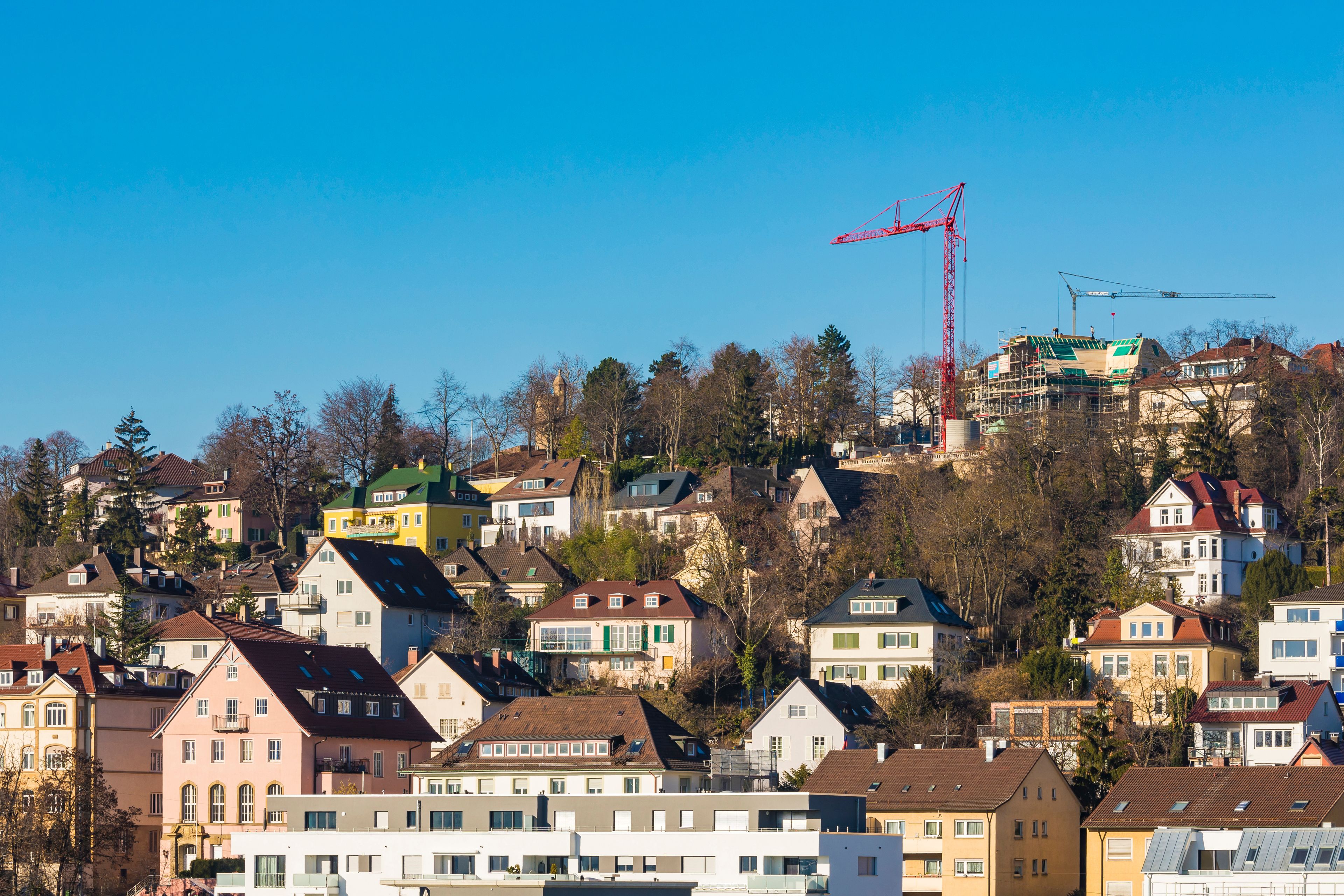 Eine Wohngegend an einem Hang mit bunten Häusern, einem markanten roten Kran und blauem Himmel.