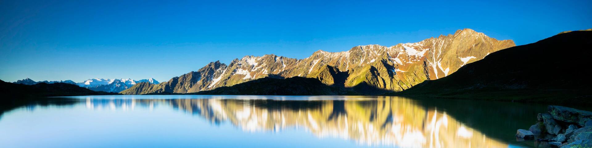 A mountain range reflected in a calm lake with clear skies.