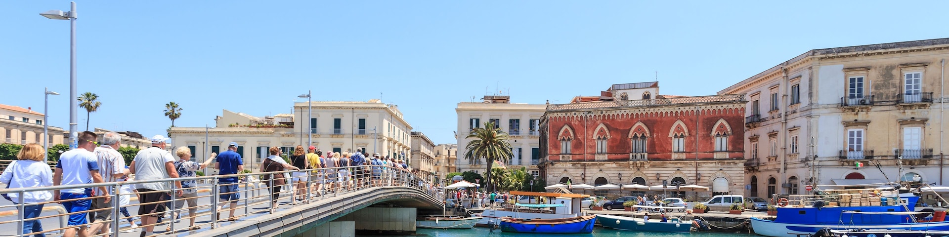 Un pont enjambant une étendue d’eau turquoise où sont amarrés des bateaux, le tout entouré de bâtiments historiques.