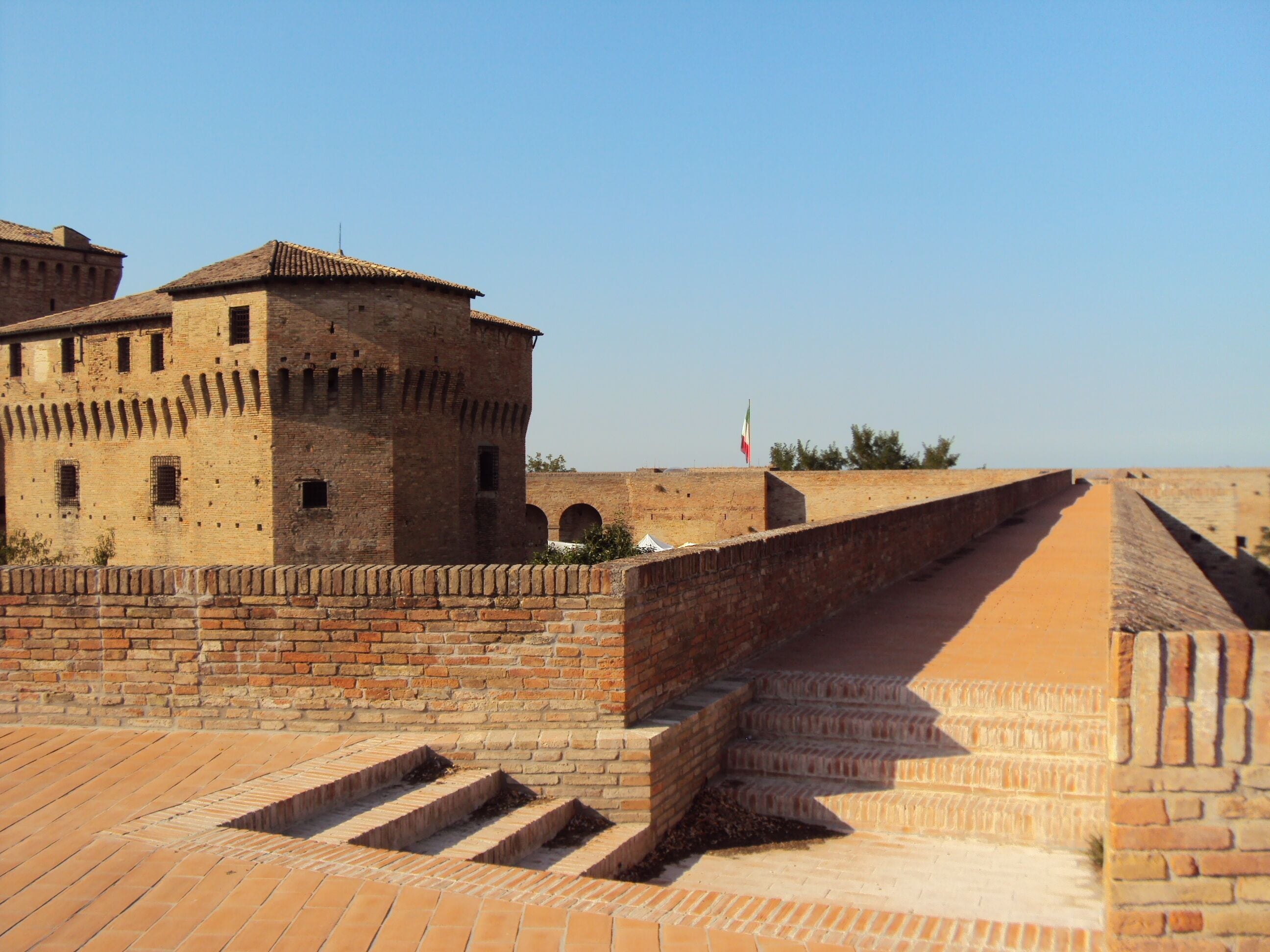 A historic stone fortress with a flagpole, arched windows, and a brick ramp leading up to the entrance.