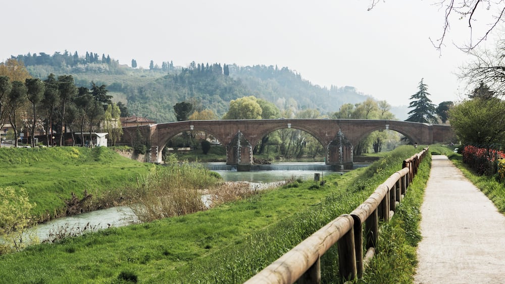 Un pont de pierre enjambant une rivière, entouré de verdure et de collines.