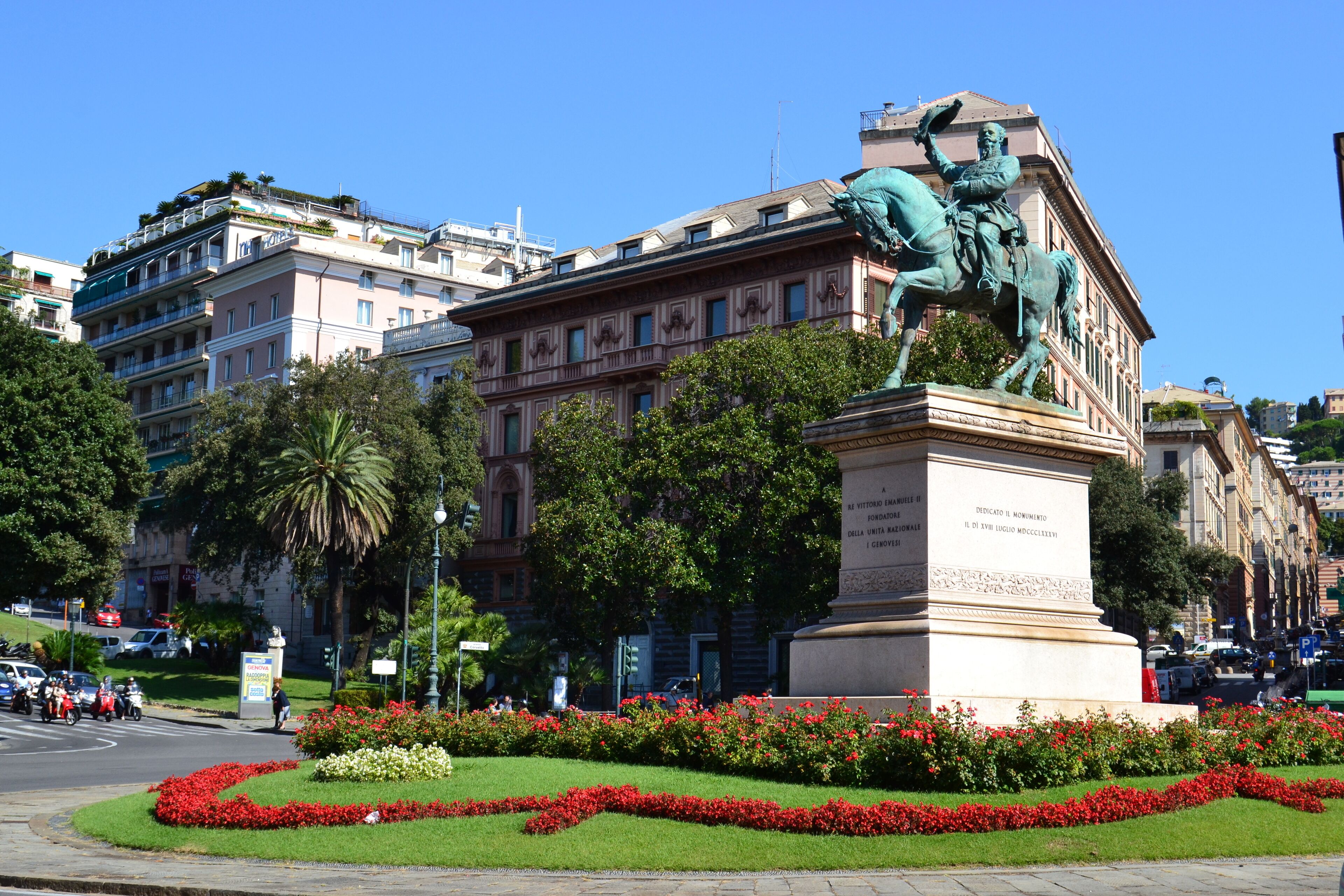 A statue of a man on a horse in front of a building with red flowers and greenery.