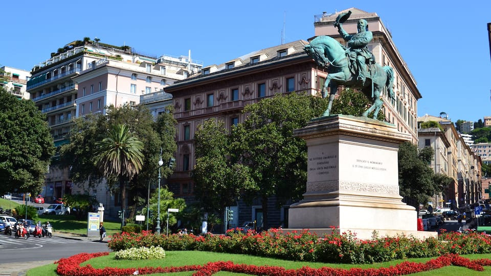 Eine Statue eines Mannes zu Pferd vor einem Gebäude mit roten Blumen und Grünpflanzen.