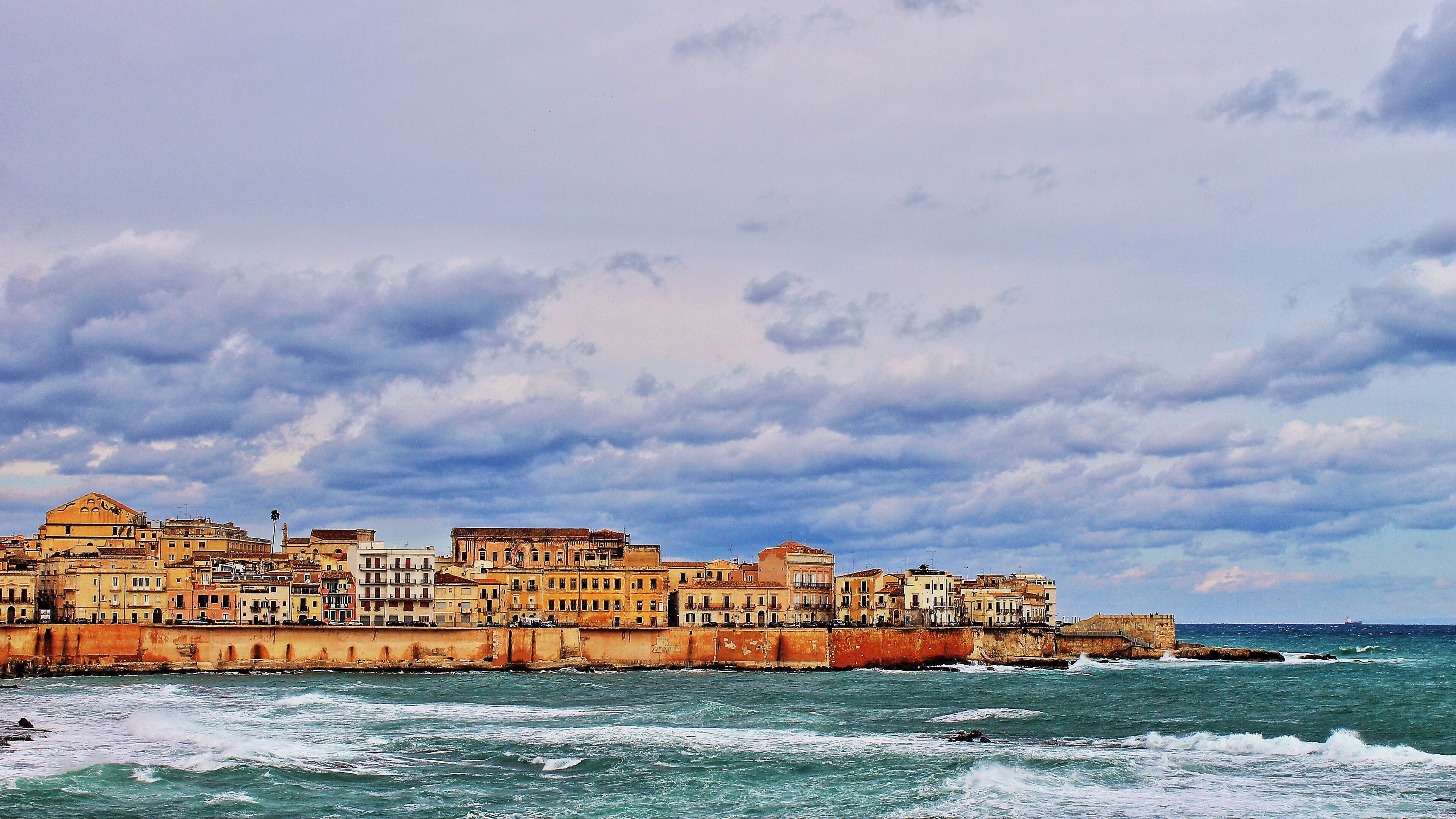 Un paysage urbain côtier avec des bâtiments historiques le long du front de mer, sous un ciel nuageux.
