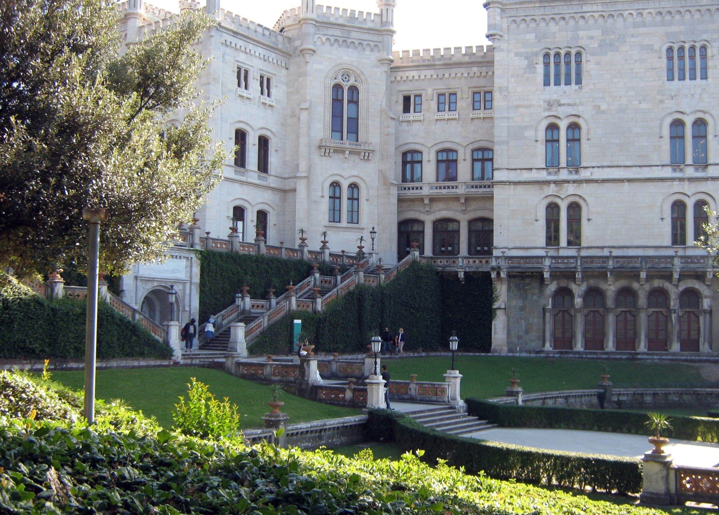 A grand building with ornate architecture, a well-maintained garden, and a staircase leading to the entrance.