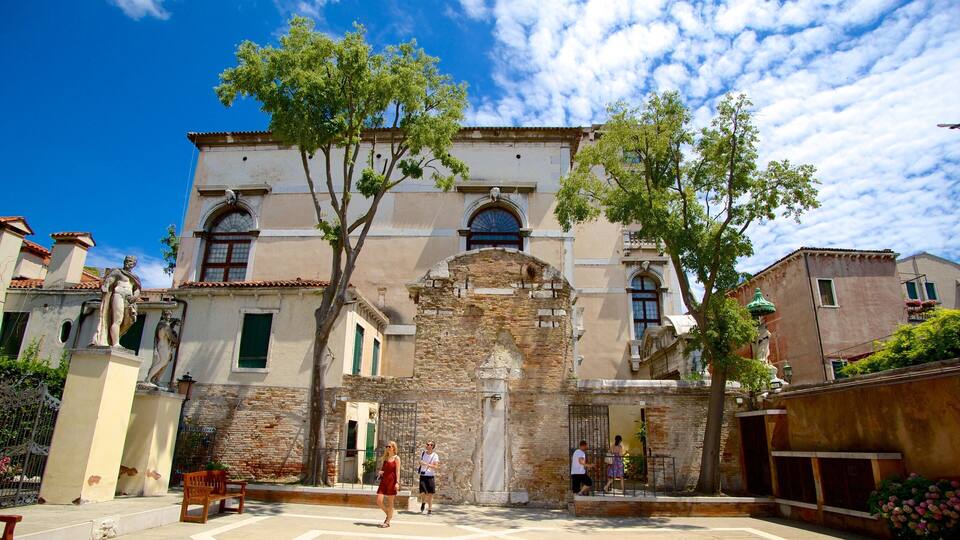 A historic building with a stone facade, arched windows, and a tree in front.