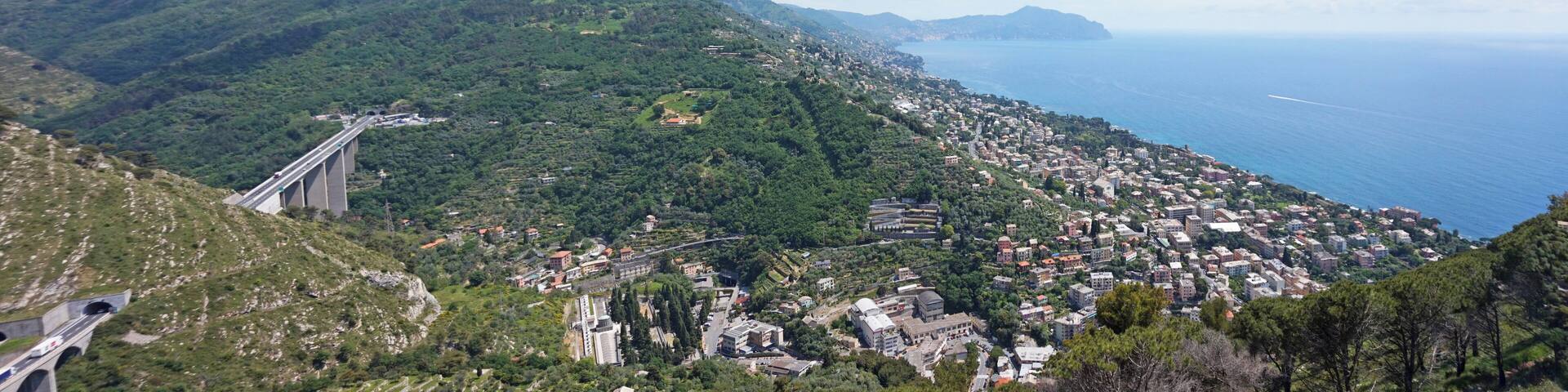 A coastal town with a bridge, lush green hills, and the sea.