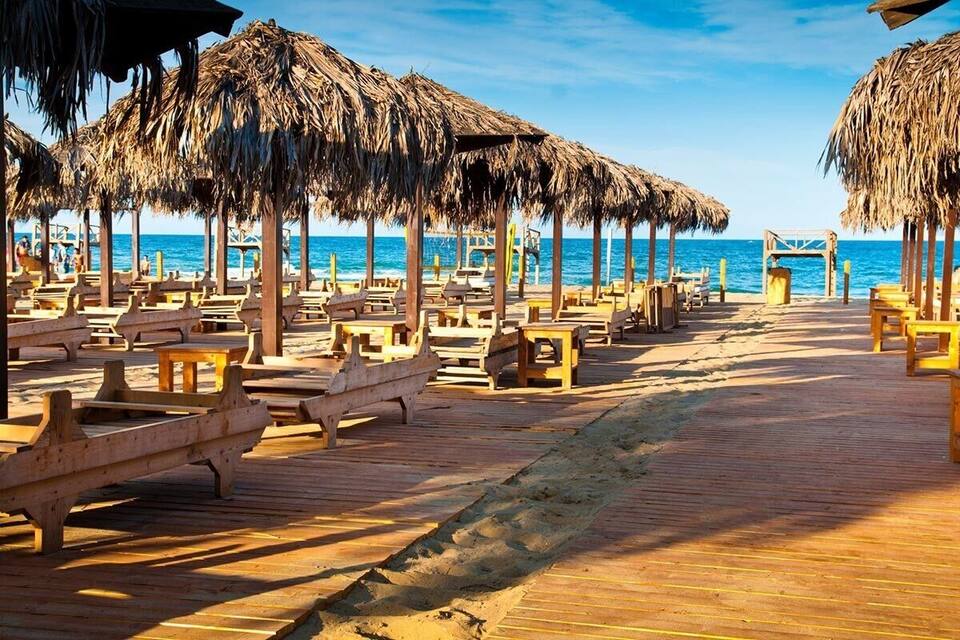 Une promenade en bois bordée de parasols en chaume et de bancs en bois, le long d’une plage.