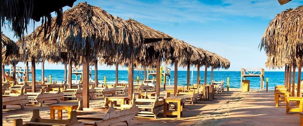 A wooden boardwalk with thatched umbrellas and wooden benches along a beach.