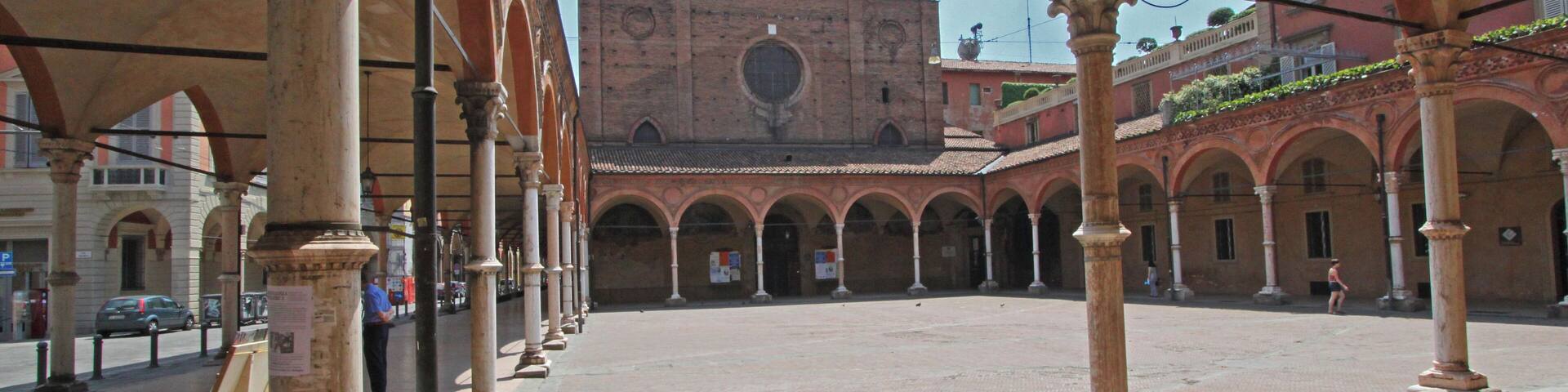 An open courtyard with arches and columns, a building with a central dome in the background, and a clear sky.