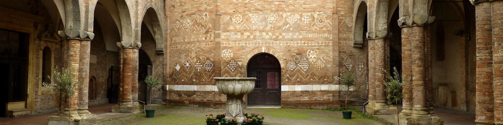Um pátio com uma fonte central, rodeado por arcos de tijolo e um muro padronizado.