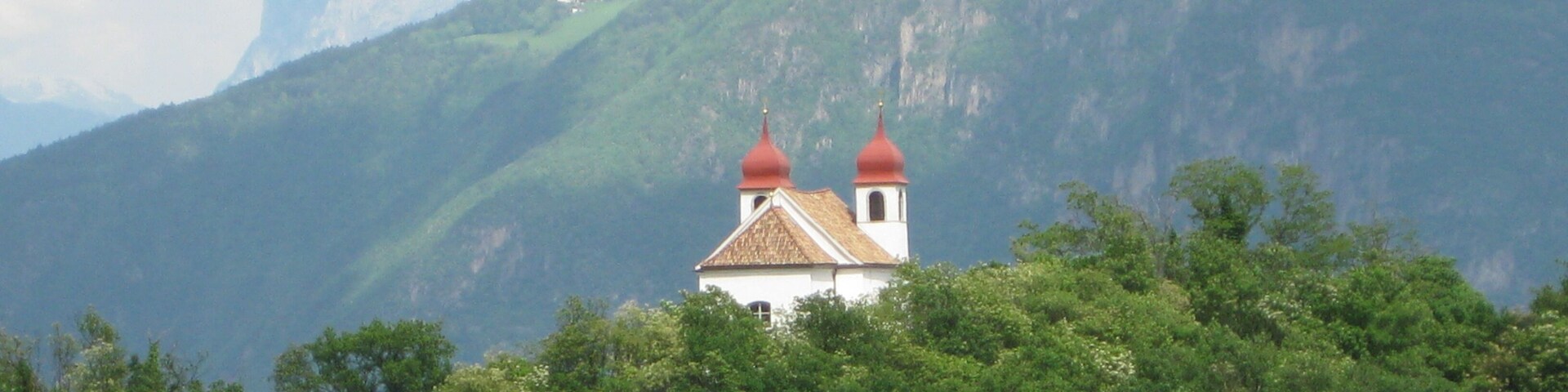 A church with red domes surrounded by lush green trees and mountains in the background.