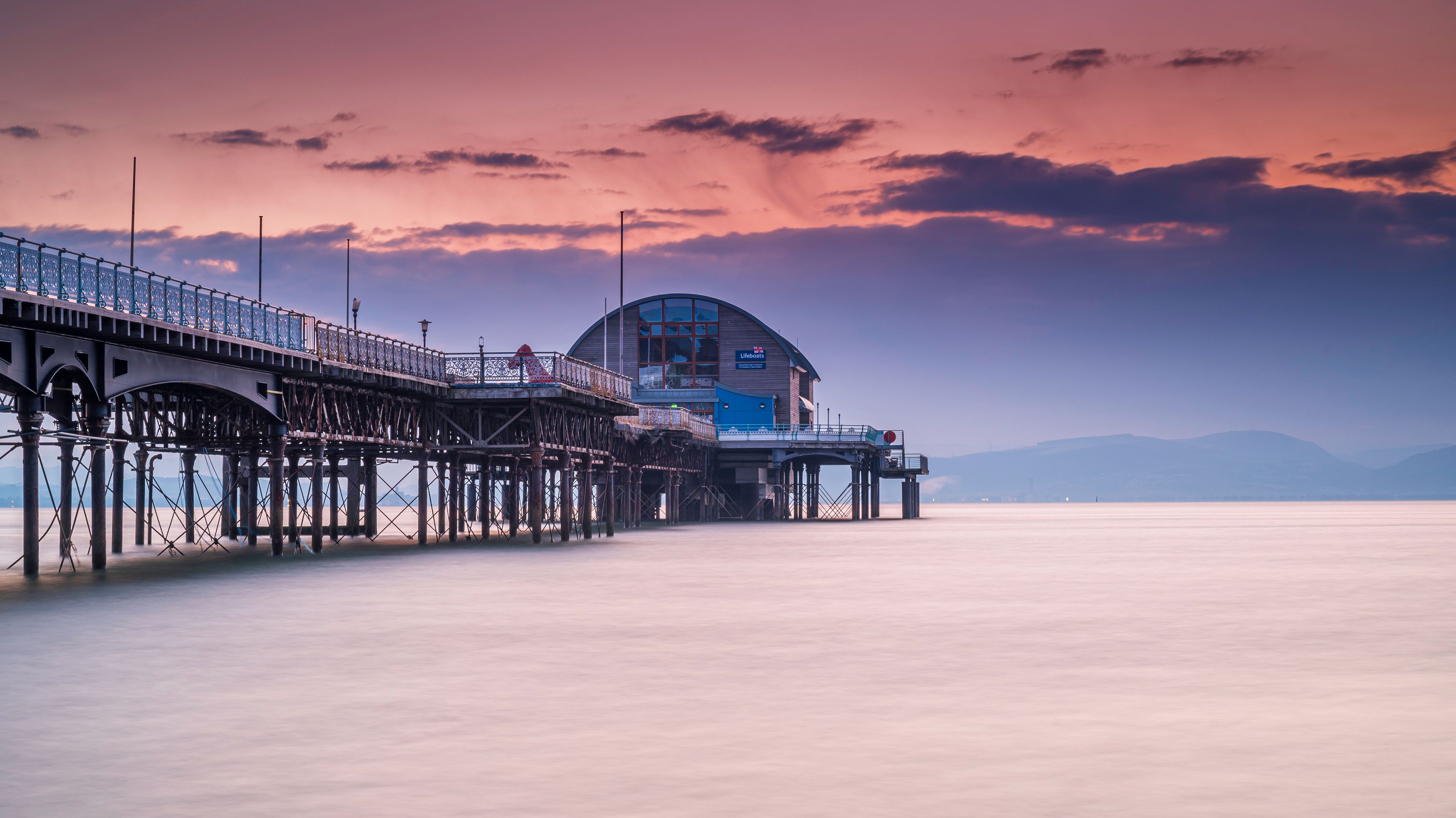 The long pier in the Mumbles, Swansea, south Wales. The wooden and steel structure sits in a calm sea, with a red sky behind it, at sunrise