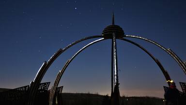 Una escultura de metal con arcos y una torre central frente a un cielo nocturno.
