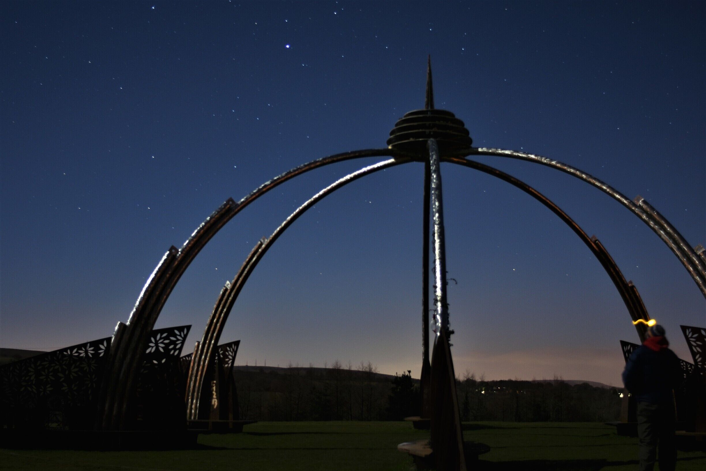 A metal sculpture with arches and a central tower against a night sky.