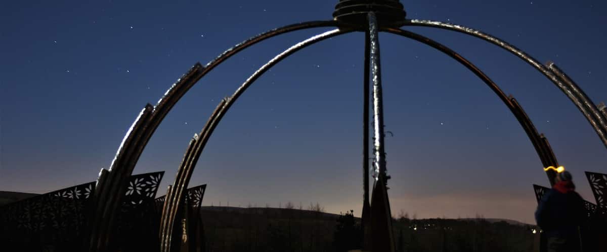 A metal sculpture with arches and a central tower against a night sky.