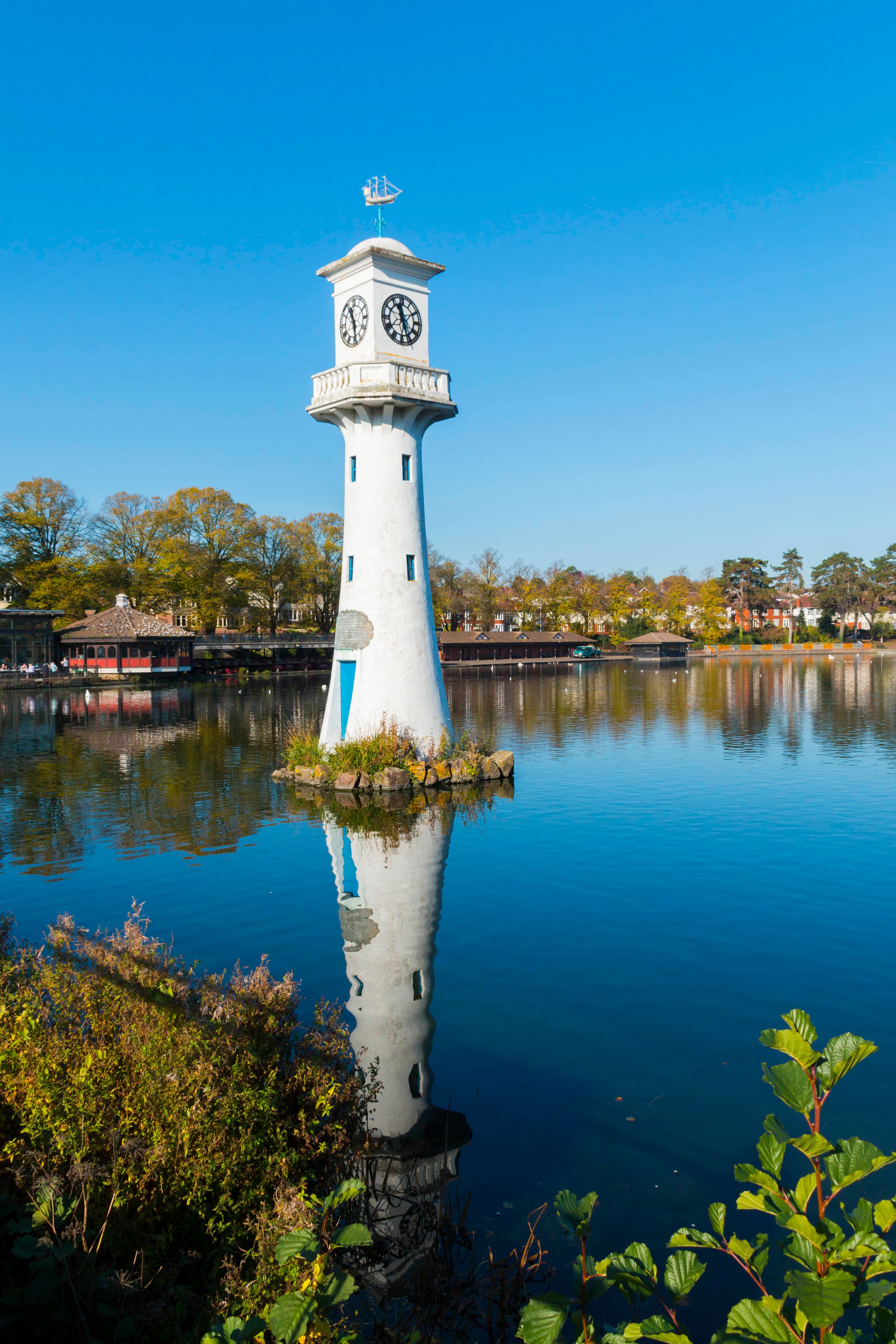 A white lighthouse with a clock tower on a small island in a calm body of water.