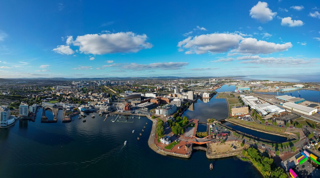 Aerial 180° Panorama Drone Shot of Cardiff Bay, Cardiff Bay Barrage, and Coastal Industrial Port with City Skyline, Waterfront Buildings, and Sunlight Reflections Under Blue Sky and Scattered Clouds,