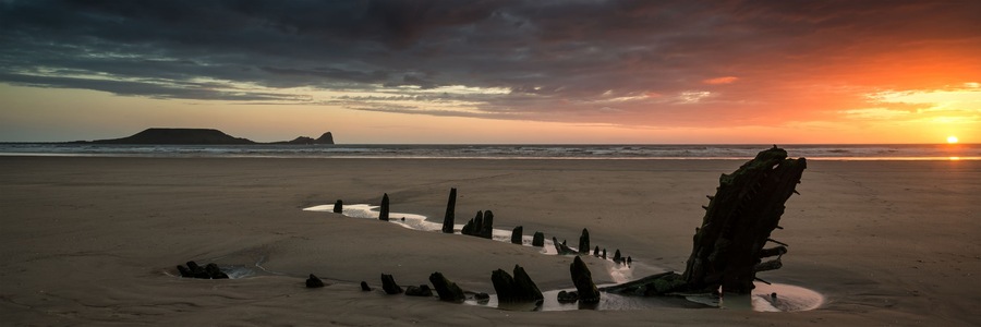 A beach with a large rock formation and a sunset in the background.