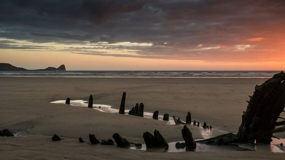 A beach with a large rock formation and a sunset in the background.