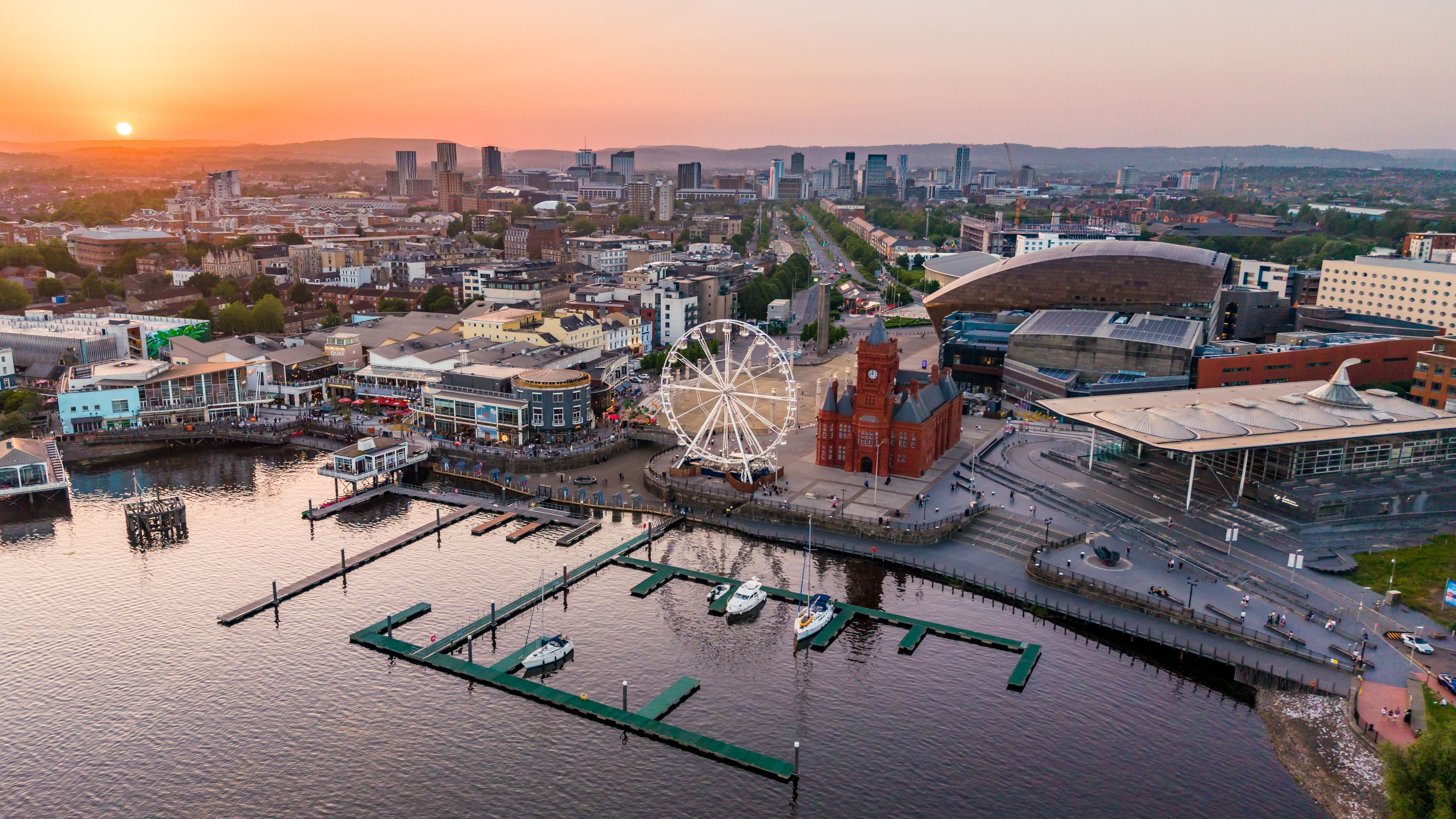 Ein Stadtbild am Wasser mit einem markanten Riesenrad, historischen Gebäuden und einem modernen Stadion.