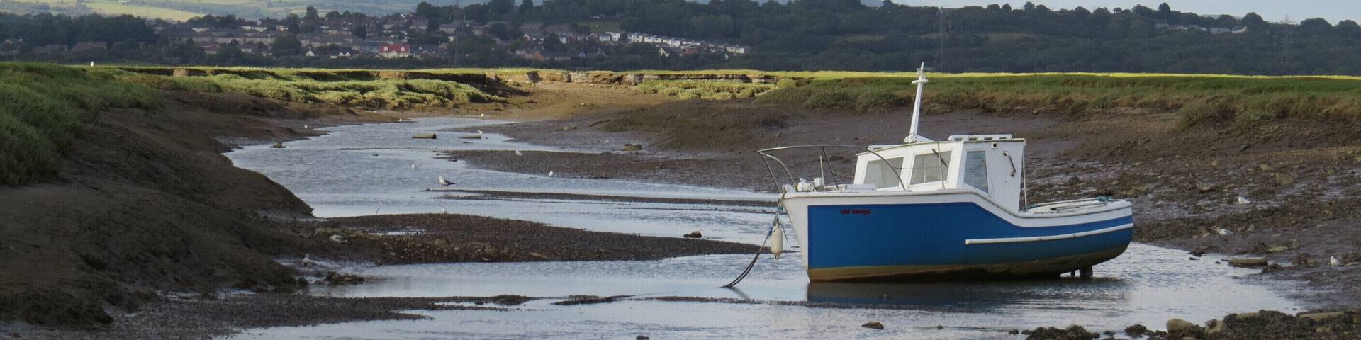 A blue boat stranded on a muddy riverbank with a town in the background.